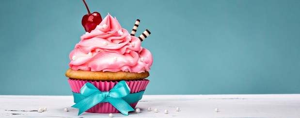 A highly decorated pink cupcake with icing and a cherry on top.