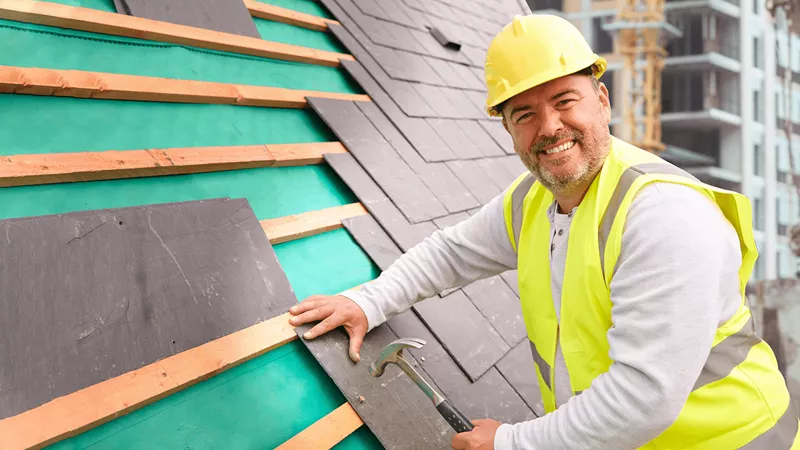 Construction worker hammering tiles to a roof.