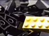 A pile of black Lego blocks with a yellow piece on top