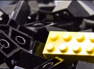A pile of black Lego blocks with a yellow piece on top
